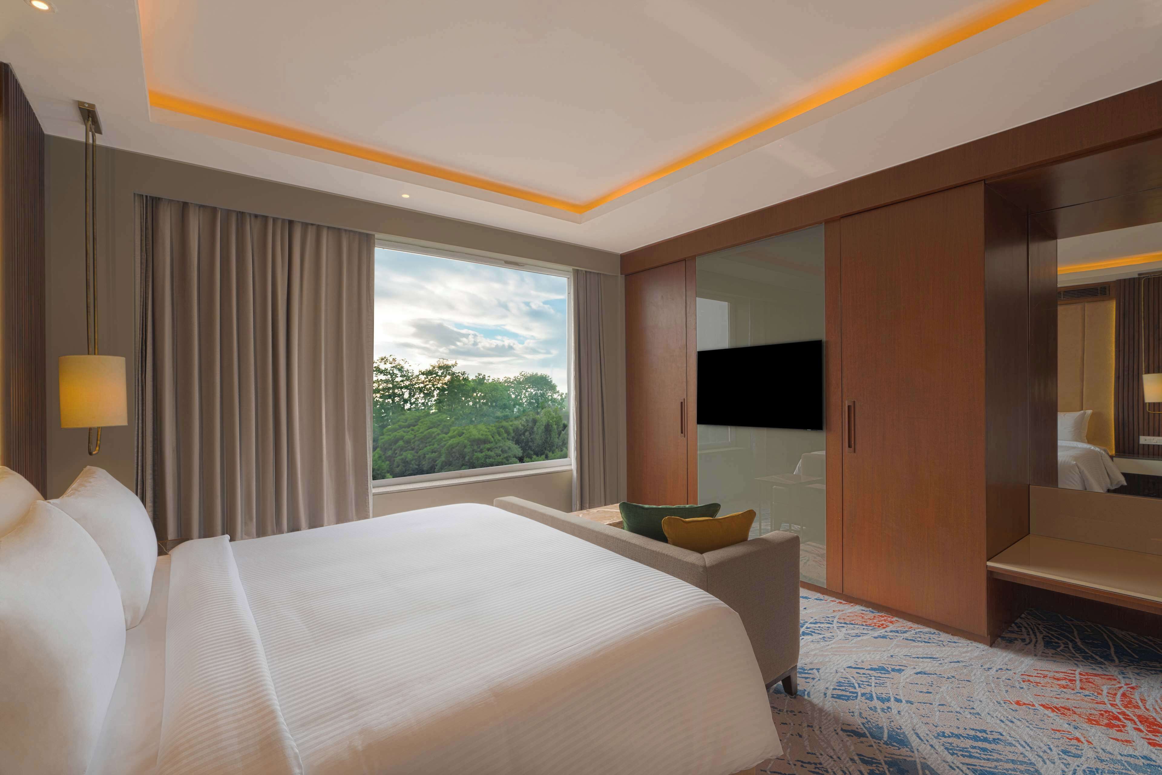 Habitación de hotel con una cama grande, un escritorio, un armario y una ventana con vistas a zonas verdes.