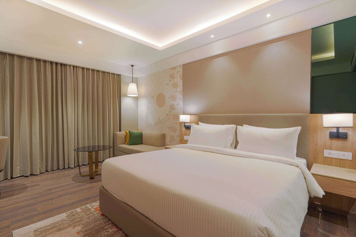 Une chambre d’hôtel moderne avec un grand lit, une petite table ronde, un canapé et une lampe.