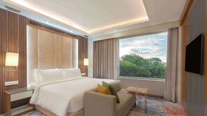 A hotel room with a large bed, a sofa, a TV, and a window with a view of trees. - Park Inn By Radisson Ayodhya (Faizabad)