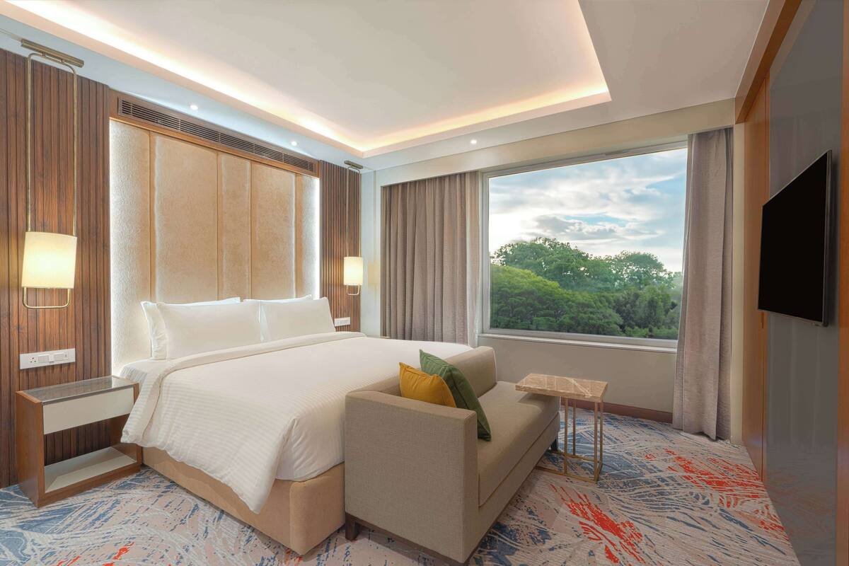 Une chambre d’hôtel avec un grand lit, un canapé, une télévision et une fenêtre donnant sur des arbres.