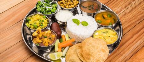 A traditional Indian meal served on a stainless steel plate with various dishes including rice, curry, and vegetables.