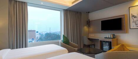 A hotel room with two beds, a desk, a chair, a TV, and a window with curtains.