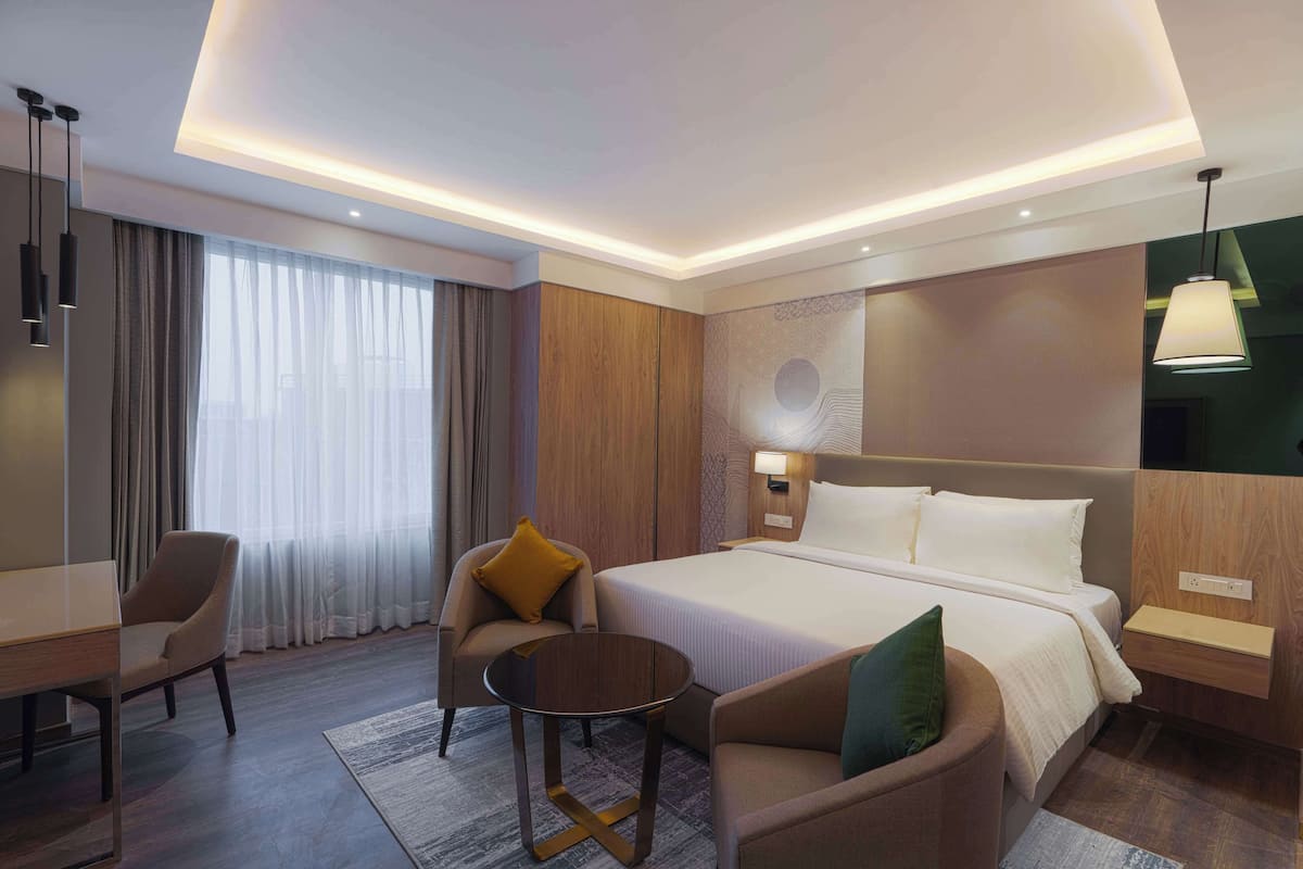 Une chambre d’hôtel comprenant un lit, deux fauteuils, une petite table, un bureau et une table de chevet.