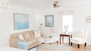 A living room with a beige sofa, a coffee table, a white armchair, and a patterned rug. - Daniel Island Getaway (Charleston)