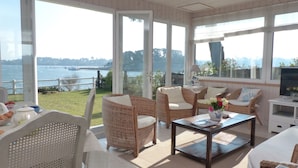 A sunlit room with wicker furniture, a coffee table, and a view of a body of water. - Maritime cottage with exceptional sea view (Baden)