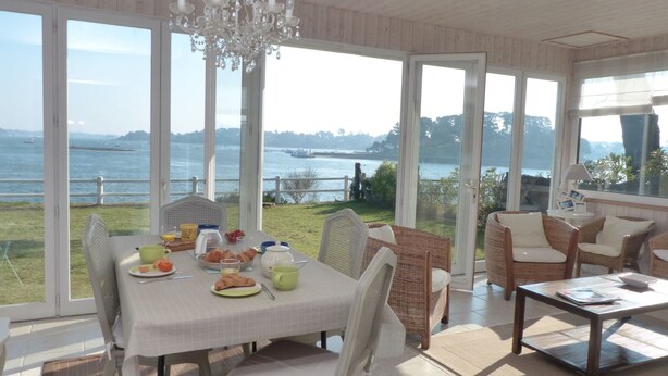 A dining area with a table set for breakfast, overlooking a body of water. - Maritime cottage with exceptional sea view (Baden)