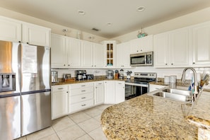 A modern kitchen with white cabinets, stainless steel appliances, granite countertops, and a built-in microwave. - Steps to Beach: Oceanside Townhome w/ Heated Pool (South Padre Island)