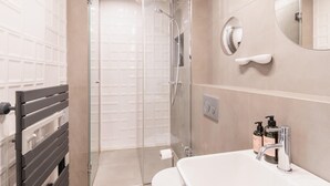 Ein modernes Badezimmer mit einer Glastrennwand zur Dusche, einem weißen Waschbecken mit Spiegel und einer Toilette.