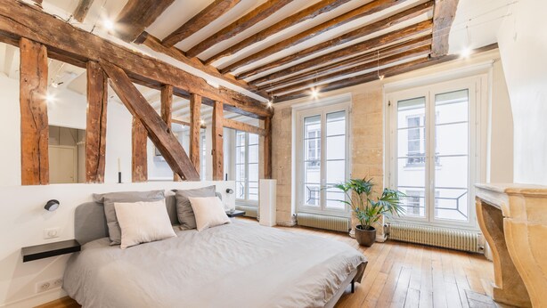 Ein Schlafzimmer mit einem großen Bett, Holzbalken, einer Topfpflanze und einem Kamin.