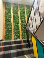 Una escalera con un muro vertical cubierto de jardín, paneles de madera y escalones de colores.