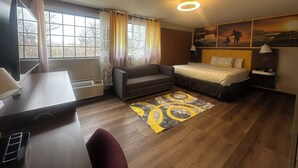 A hotel room with a bed, a desk, a chair, a sofa, and a window with curtains.