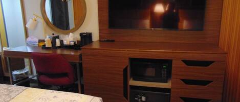 A hotel room with a wooden desk, a television mounted above it, a microwave built into the desk, a red chair, and two beds with floral bedspreads.