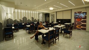 A restaurant with a modern interior, featuring a woman seated at a table. - Blue Diamonds Inn (Greater Noida)