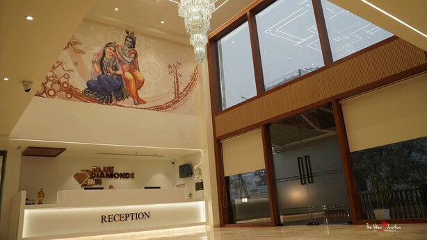 A hotel reception area with a mural, a chandelier, and a reception desk labeled "RECEPTION". - Blue Diamonds Inn (Greater Noida)
