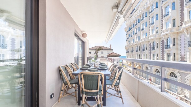 Un balcón con mesa para cuatro, sillas de mimbre y vista a un paisaje urbano con edificios históricos.