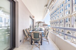 A balcony with a dining table set for four, surrounded by wicker chairs, overlooking a cityscape with historic buildings. - A short stroll to Palais/Beach, Terrace & Seaview (Cannes)