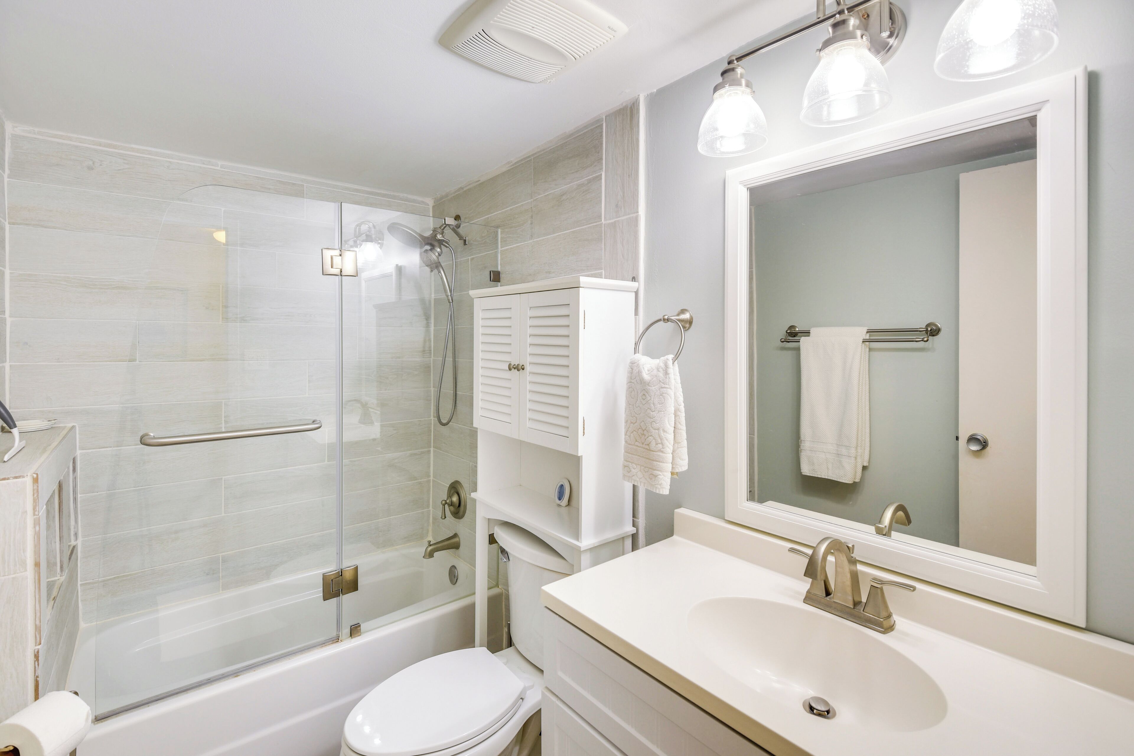 Une salle de bain moderne avec une douche à parois de verre, des toilettes blanches, un lavabo avec un miroir et un porte-serviettes.