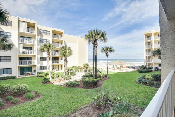 A courtyard with a pool, palm trees, and a view of the ocean. - New Smyrna Beach Condo w/ Ocean-View Balcony! (New Smyrna Beach)