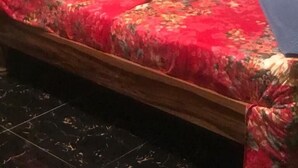 Una cama con colcha y almohadas estampadas con motivos florales, cabecera de madera y paredes verdes.