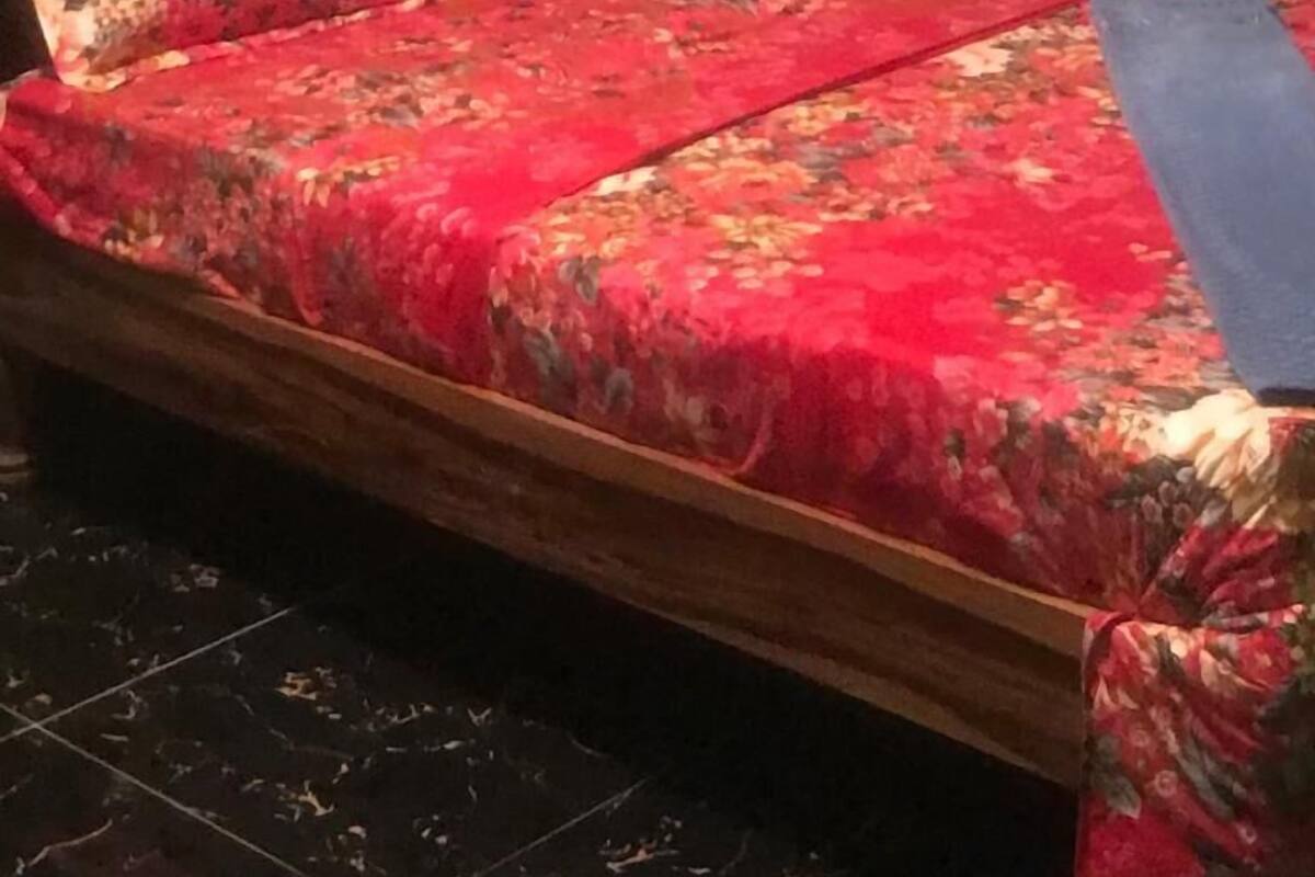 Ein Bett mit blumigem Bettbezug und Kissen, ein Holz-Kopfende und grüne Wände.