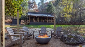 Un foyer extérieur entouré de quatre chaises Adirondack, une terrasse en bois et un chalet en arrière-plan.
