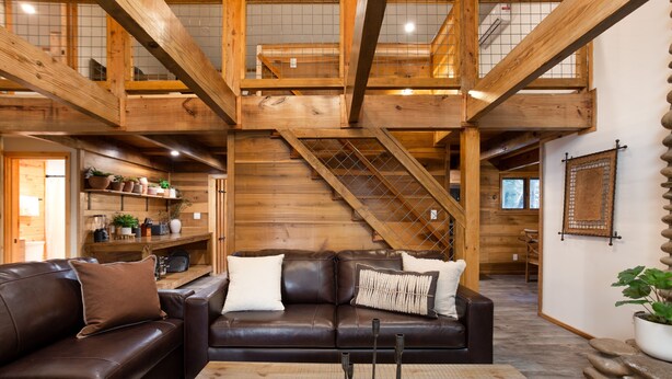 Un vaste espace de vie comprenant un canapé en cuir marron, une table basse en bois et un escalier menant à un niveau supérieur.