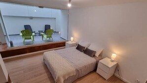 Ein Schlafzimmer mit einem großen Bett, Nachttischen mit Lampen, einem Spiegel und Blick auf einen Balkon mit Sitzgelegenheiten.