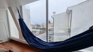 Eine Hängematte in einem Zimmer mit großen Fenstern, Holzboden und Blick auf Gebäude.