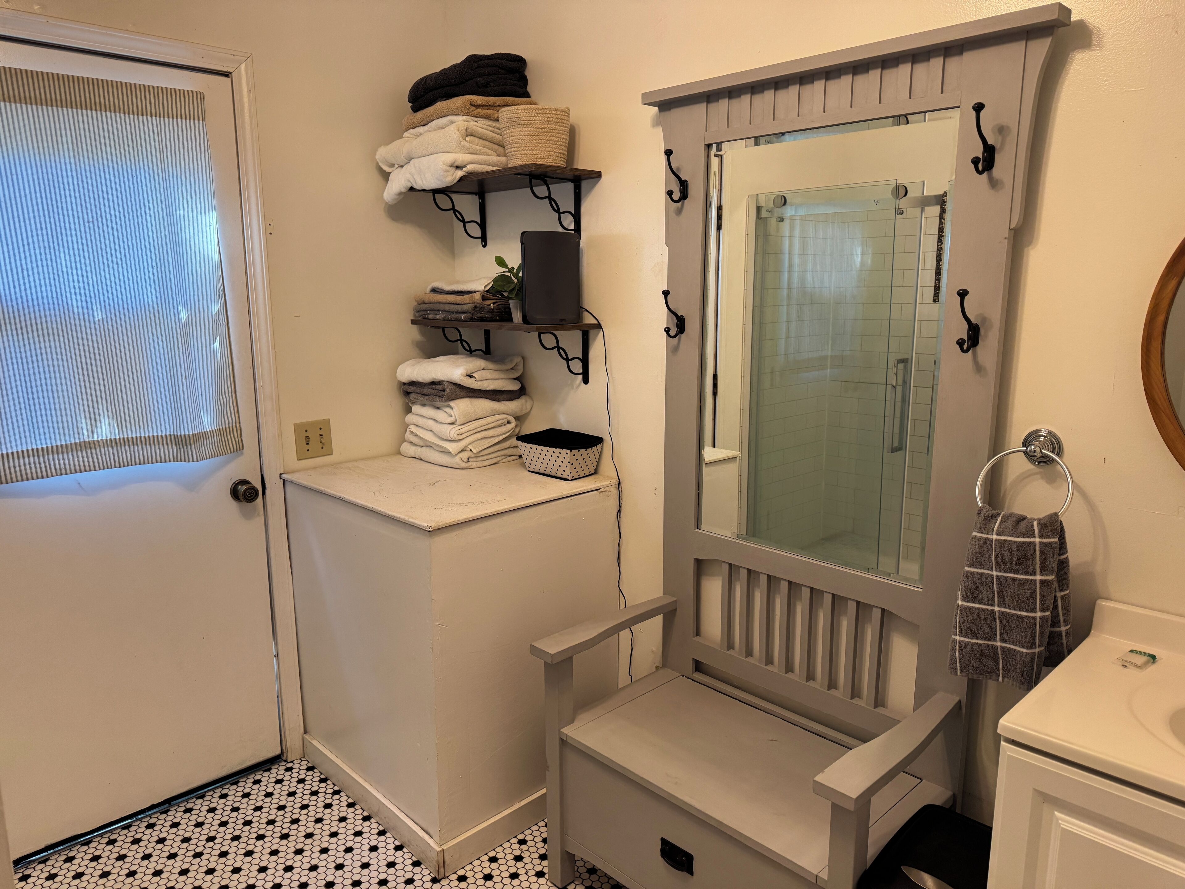 A bathroom with a white sink, a mirror, a towel rack, and a shelf with folded towels.