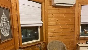 A cozy room with wooden walls, two wicker chairs, a small table with a vase, and an air conditioning unit mounted on the wall. - Stay on the farm - 1 bedroom cottage with deck outside of Davis (Davis)