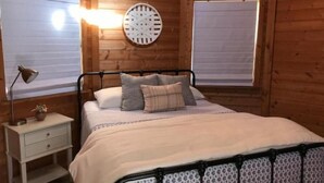 A wooden cabin bedroom with a bed, bedside lamp, and a wall clock. - Stay on the farm - 1 bedroom cottage with deck outside of Davis (Davis)