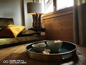 Uma sala de estar acolhedora com piso de madeira, um sofá verde, uma almofada amarela, um abajur e uma bandeja com tigelas.