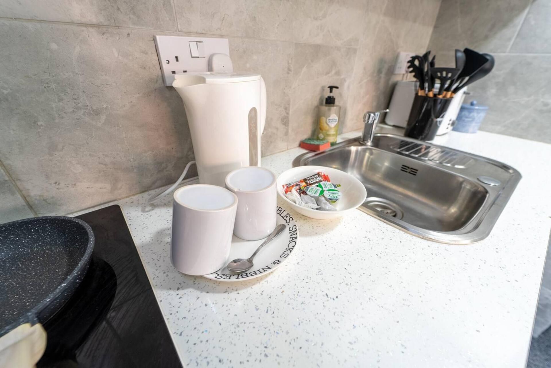 Eine Küchenarbeitsplatte mit Spüle, einer Kaffeemaschine, einer Schüssel mit Snacks und einem Teller mit einem Löffel.