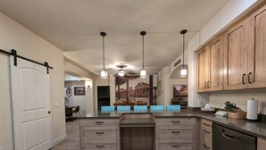 A modern kitchen with wooden cabinets, a central island with blue seating, pendant lighting, and a dishwasher. - The Hideout is a recently remodeled, fully wheelchair-accessible, luxury condo  (St. George)