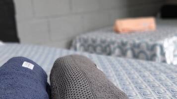 A neatly made bed with a blue and white patterned bedspread, a folded gray blanket, and a folded blue blanket.