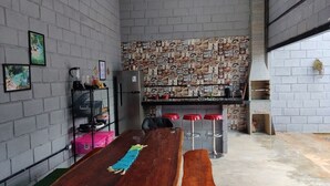 A compact kitchen with a brick wall backsplash, a wooden table, and a bar area with stools. - Suíte maravilhosa Casa da Serra (Aurora do Tocantins)