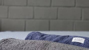 A bed with a gray blanket and a blue patterned blanket, both labeled 'CASA RIACHUELLO'.