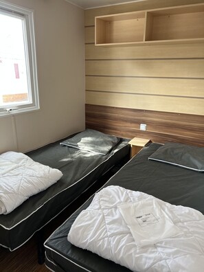 A room with two single beds, a wooden headboard, a window, and a built-in shelf. - Mobilhome Ca61 Camping 4 Vias Plage 6/8 Personnes (Vias)