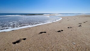 A beach with footprints leading to the water, a clear sky, and waves approaching the shore. - Stunning 2BR/2BA Bayfront Retreat (Ocean City)