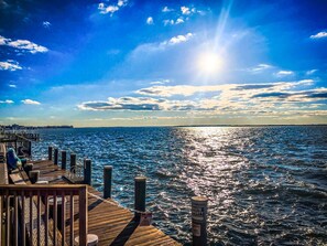 Une jetée en bois s’étendant dans une étendue d’eau, sous un ciel dégagé et un soleil brillant.