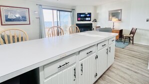 A modern kitchen with a large island, wooden chairs, a television, and a view of the sea. - Stunning 2BR/2BA Bayfront Retreat (Ocean City)
