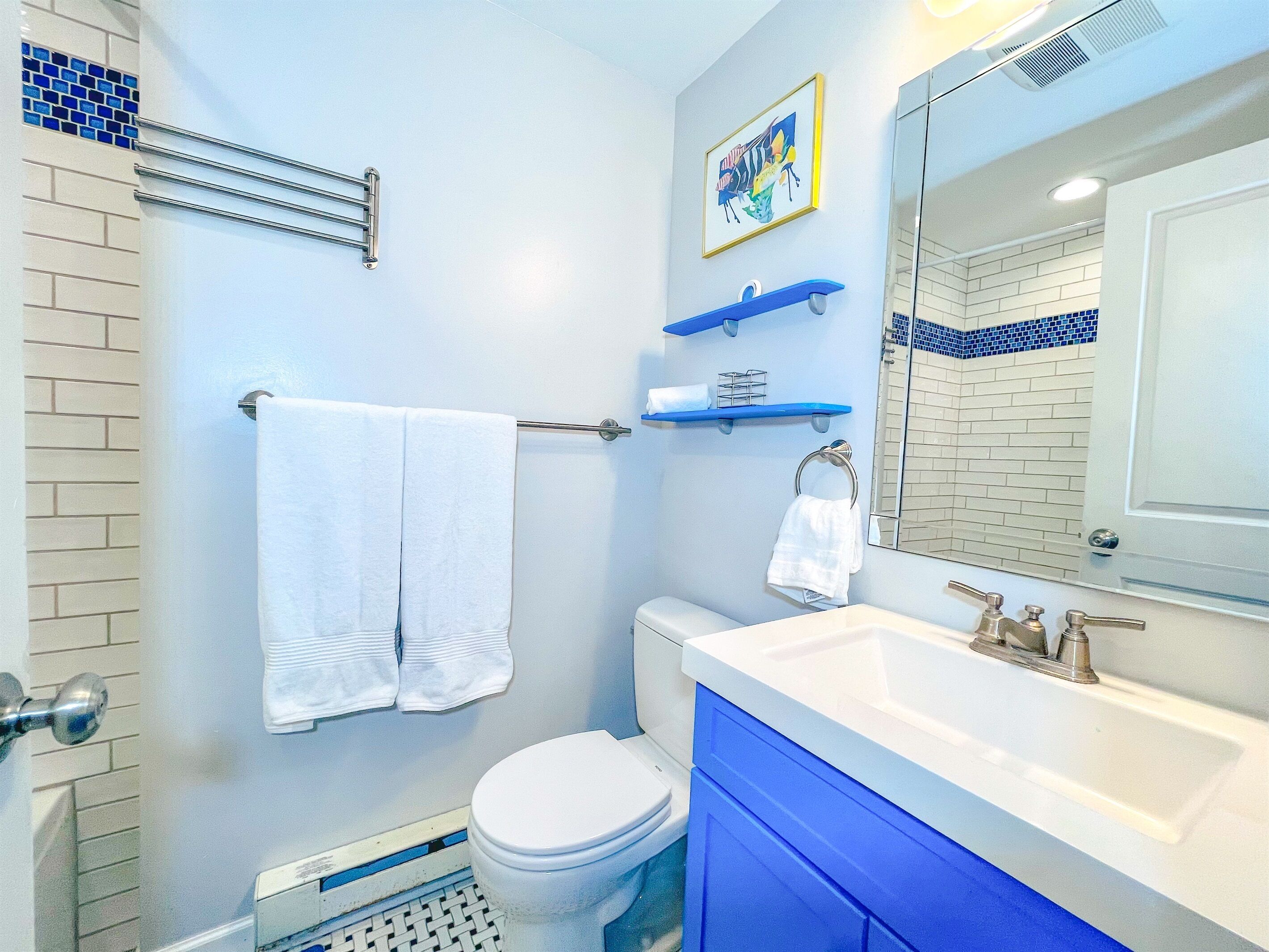 A bathroom with a white toilet, a sink with a mirror, and blue cabinets.