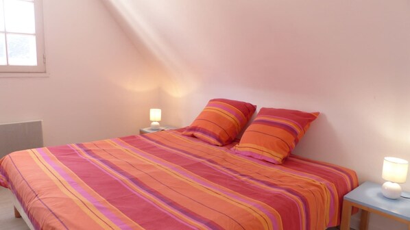 A bed with a striped bedspread and two pillows, two bedside lamps, and a window with blinds.
