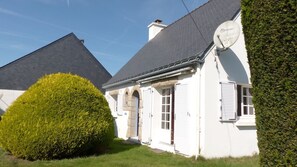 A white building with a black roof, a satellite dish, and a well-maintained hedge.