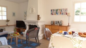 Ein Wohnzimmer mit Fernseher, Korbmöbeln, einem Esstisch mit Frühstücksangebot und einem Kamin.