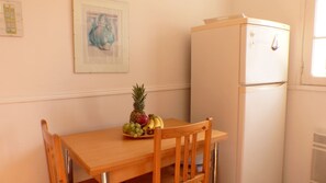 Ein kleiner Essbereich mit einem Holztisch, einem Stuhl, einem Kühlschrank und einem Wandbild.