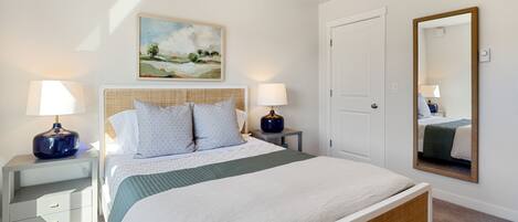Un dormitorio ordenado con una cama grande, dos mesitas de noche con lámparas, un cuadro en la pared, una puerta y un espejo.