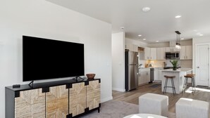 A modern kitchen with a flat-screen TV, wooden cabinets, and a central island with stools.
