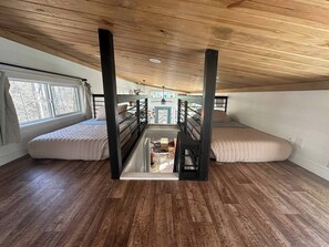 A loft bedroom with a high ceiling, wooden beams, a glass floor, and two large bean bag chairs. - Blueberry Farm Cottage | Hot Tub, Creek, Game Room (Mentone)