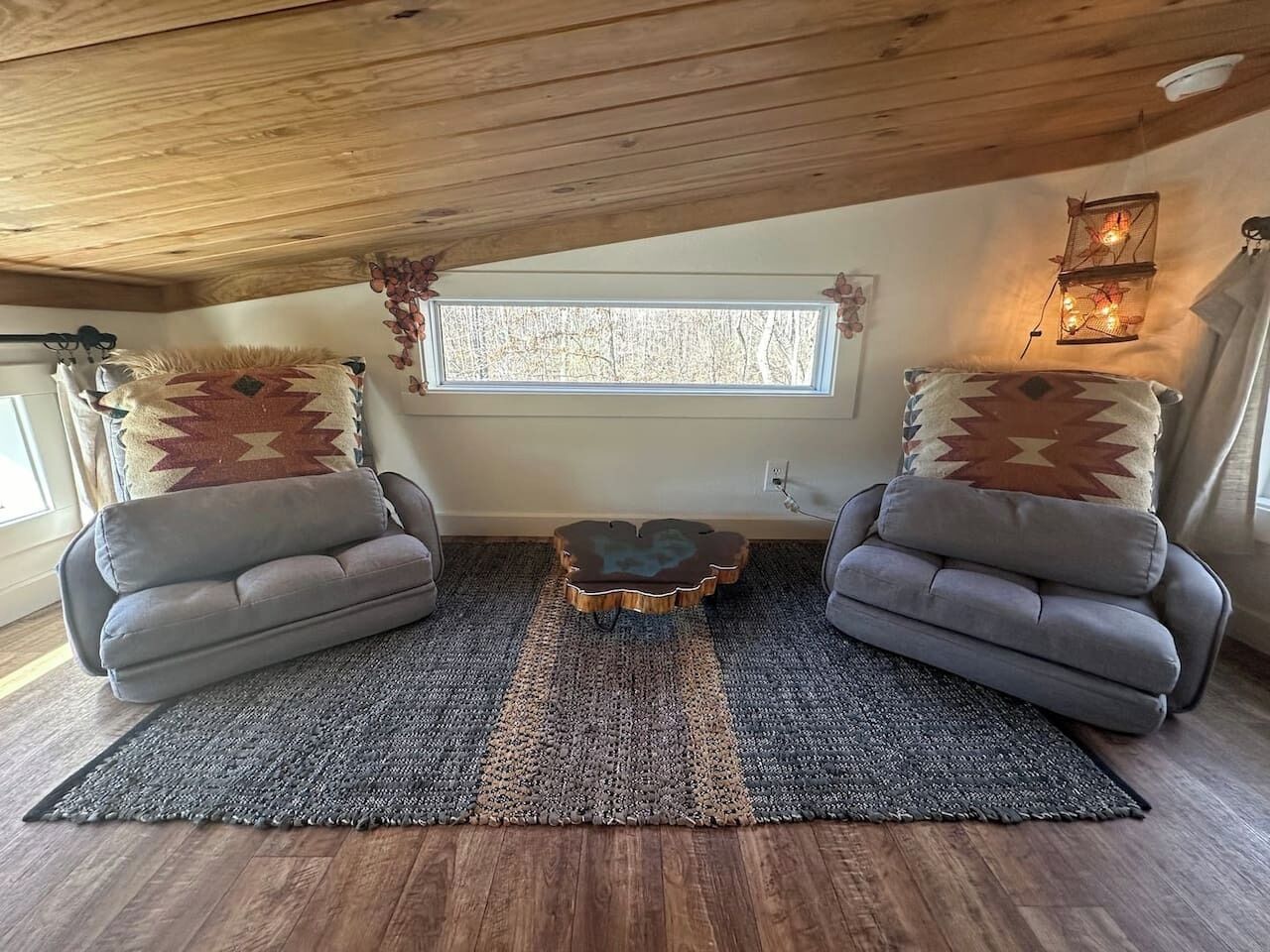 A cozy room with a wooden ceiling, two gray sofas with patterned cushions, a woven rug, and a small round table.